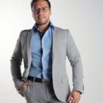 Confident man in grey suit and blue shirt poses for a professional portrait.